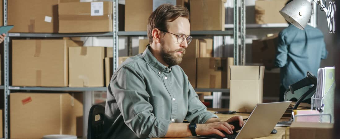 Hombre mirando una computadora con inventario detrás de él